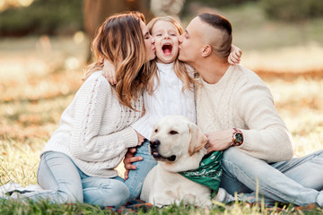 Happy beautiful family with dog labrador is having fun  are sitting on green grass in park.