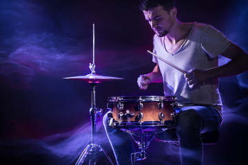 A drummer plays drums on a blue background. Beautiful special effects of light and smoke. The process of playing a musical instrument.