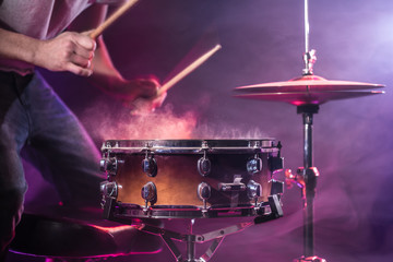The drummer plays the drums. Beautiful blue and red background, with rays of light. Beautiful special effects smoke and lighting. The process of playing a musical instrument. Close-up photo.