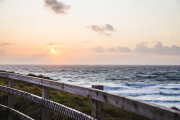 Obraz premium Lovely Beautiful Sunset in Cornwall England waves crashing against the base of the tall dangerous cliffs, fenced off to prevent suicide of young people or accidental death from falling.