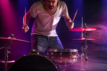 The drummer plays the drums. Beautiful blue and red background, with rays of light. Beautiful special effects smoke and lighting. The process of playing a musical instrument. Close-up photo.