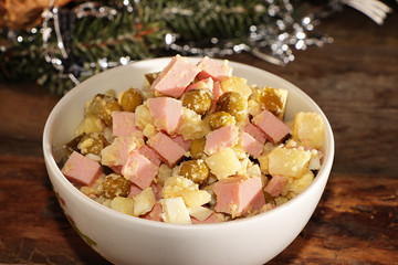 Traditional Russian salad Olivier from peas, cucumbers, potatoes, eggs and sausages on an old wooden table, selective focus, rustic style, close-up