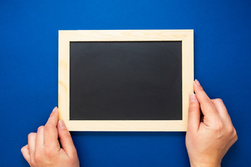 Chalkboard mock up. Female hands holding blackboard on a blue background, isolated. Copy space, flat lay. Business, education concept.