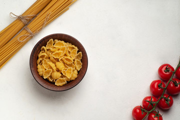 Raw pasta in a plate next to long pasta and a branch of cherry tomatoes symmetry top view free space