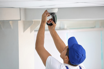 Technician installing CCTV camera on ceiling indoors