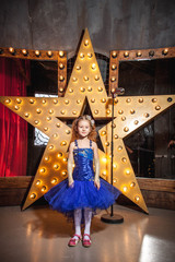 girl in blue puffy dress at the microphone with a big star in the background