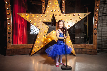 girl in blue puffy dress at the microphone with a big star in the background
