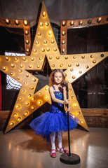 girl in blue puffy dress at the microphone with a big star in the background