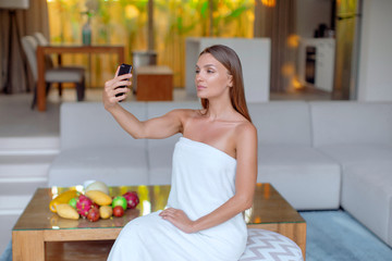 Young beautiful girl with a smartphone takes a selfie in the morning and talks on the Internet.