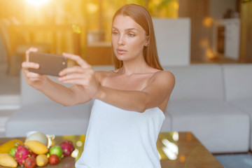 Young beautiful girl with a smartphone takes a selfie in the morning and talks on the Internet.