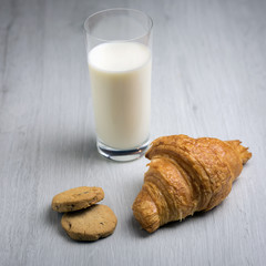 A croissant, some cookies and a glass of milk