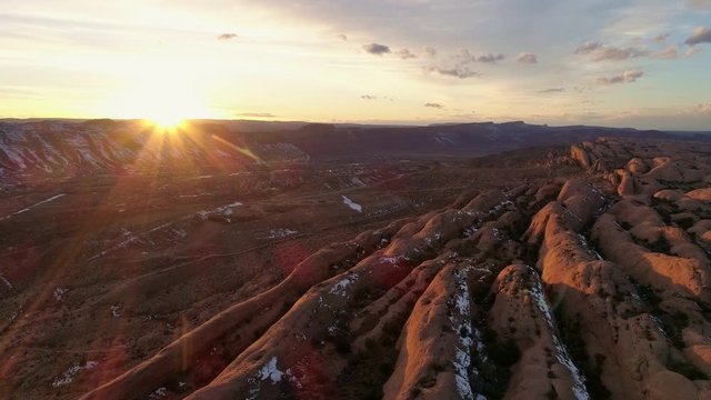 The sun lighting up desert red rock cliffs as it sets in the horizon over Moab Utah.