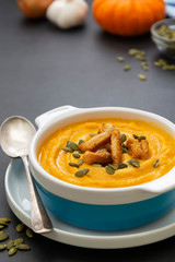 Creamy carrot soup, autumn foods. Spicy, roasted vegetable soup in bowl. Dark background.