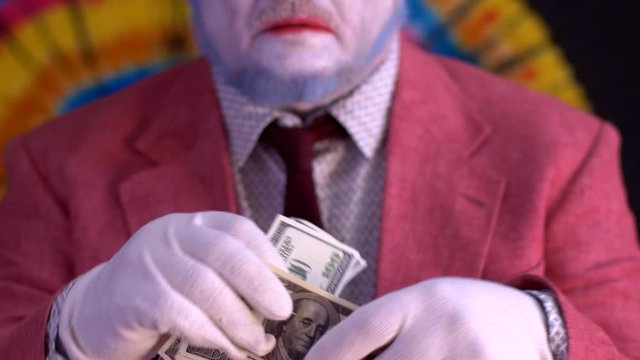 elderly mime man in large glasses with blue hair and beard in bright pink jacket and tie in white gloves. clown takes out pack of money from his pocket, recounts it and puts it back. Happy clown