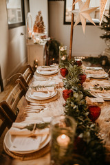Christmas table setting for traditional lunch or dinner on a rustic table with seasonal greeting cards, tableclothes, tableware and festive decorations. Concept of family traditions and celebrations