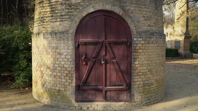 Brick water tower against blue sky. Old round tower with wooden door on lock. Tower in the vine. Tale of the imprisonment of the princess. Mystical place. 