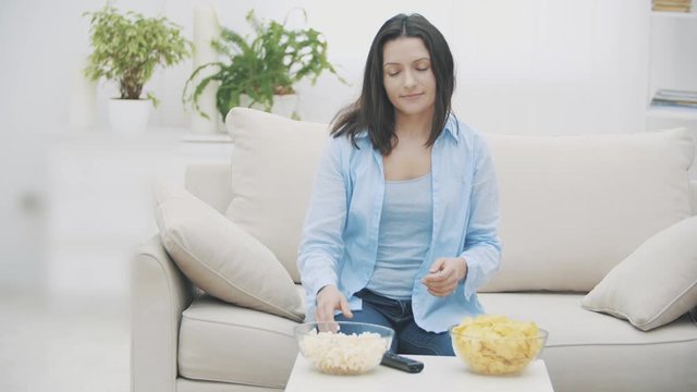 Slowmo. Happy woman switches TV on with a zapper and takes a huge deep plate with pop corn. 4K.