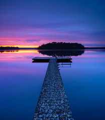 Wooden Pier into calm lake covered by fallen leaves  in autumn after sunset