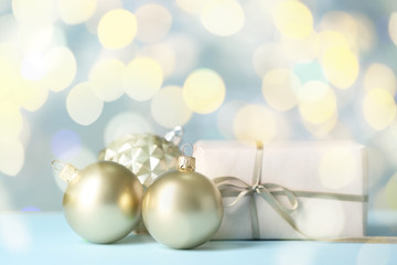 Beautiful Christmas balls with gift on table against blurred lights