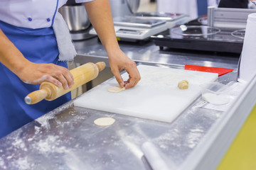 Professional cooking, catering, culinary, gastronomy and food concept. Baker, chef hands preparing fresh dough with rolling pin on kitchen table at cuisine of restaurant, bakery