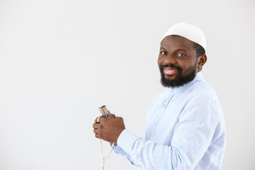 African-American Muslim man with Koran and beads on light background