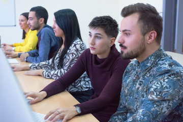 Group of  university IT technologies students working on practice lessons. Sitting near therir computer and looking for solution during class.