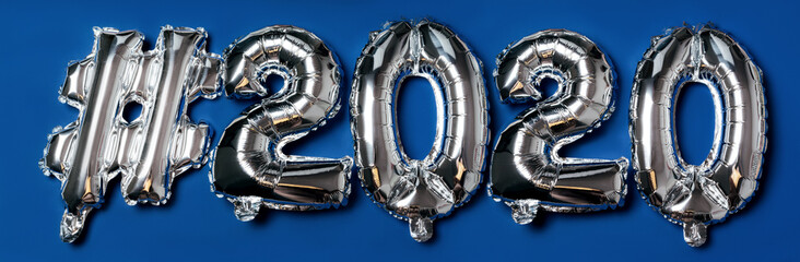 The inscription of the air inflatable foil balloon glossy hashtag letters 2020 on a blue background. Banner in classic trend color. Flat lay new year concept