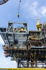 Fototapeta premium Offshore crane on board a construction work barge performing heavy lifting of a frame strcuture from a work barge at oil field