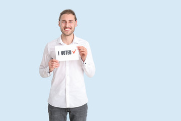 Young man holding paper with text I VOTED on color background