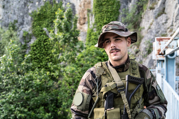 Special force military soldier portrait smiling in battle zone or military practice wearing combat uniform and hat on the bridge in nature guard patrol