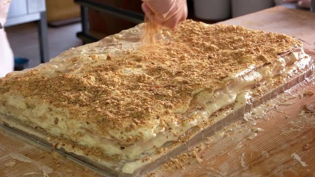 Confectioner preparing layered cake. Pastry chef decorating napoleon cake with biscuit crumbs. Best recipe of puff dough cake.