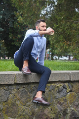 Obraz premium Portrait of a guy in a shirt sitting in a park in a European city. A man in the background of trees and buildings. Stock photos