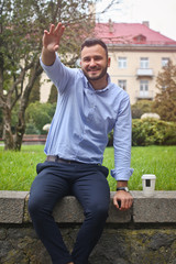 Portrait of a guy in a shirt sitting in a park in a European city. A man is greeted with other people against the background of trees and buildings. Stock photos