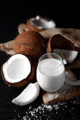 fresh coconut milk in a glass against a dark background, coconut cosmetic cream, milkshake with coconut slices