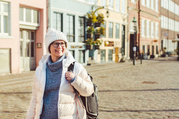 Portrait of a young Caucasian European woman tourist in glasses for the view of a white hat and a down jacket with a black backpack posing on an old Europe street in the city of Copenhagen in Denmark