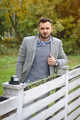 Portrait of a sexy man dressed in a suit. Fashionable guy in the autumn nature near a white wooden fence. Businessman relaxes. Skok photo for design © snb2087
