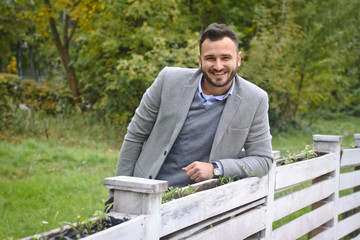 Portrait of a sexy man dressed in a suit. Fashionable guy in the autumn nature near a white wooden fence. Businessman relaxes. Skok photo for design © snb2087