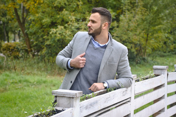 Portrait of a sexy man dressed in a suit. Fashionable guy in the autumn nature near a white wooden fence. Businessman relaxes. Skok photo for design © snb2087