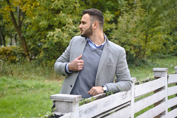 Portrait of a sexy man dressed in a suit. Fashionable guy in the autumn nature near a white wooden fence. Businessman relaxes. Skok photo for design © snb2087