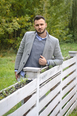 Portrait of a sexy man dressed in a suit. Fashionable guy in the autumn nature near a white wooden fence. Businessman relaxes. Skok photo for design © snb2087
