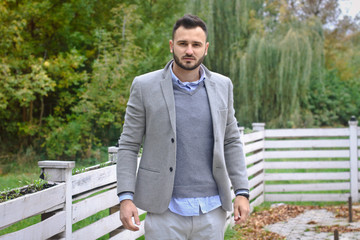 Portrait of a sexy man dressed in a suit. Fashionable guy in the autumn nature near a white wooden fence. Businessman relaxes. Skok photo for design © snb2087