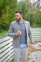 Portrait of a sexy man dressed in a suit. Fashionable guy in the autumn nature near a white wooden fence. Businessman relaxes. Skok photo for design © snb2087