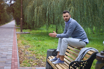 Fototapeta premium Young sexy guy sitting on a bench in an autumnal, summer park. A man contemplating new ideas while walking. European countryside. Stock Photo