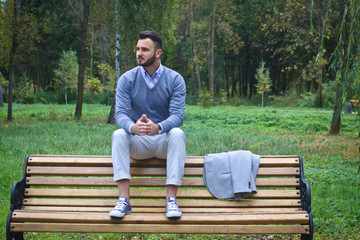 Fototapeta premium Young sexy guy sitting on a bench in an autumnal, summer park. A man contemplating new ideas while walking. European countryside. Stock Photo