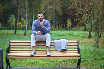Fototapeta premium Young sexy guy sitting on a bench in an autumnal, summer park. A man contemplating new ideas while walking. European countryside. Stock Photo