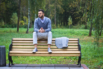 Fototapeta premium Young sexy guy sitting on a bench in an autumnal, summer park. A man contemplating new ideas while walking. European countryside. Stock Photo