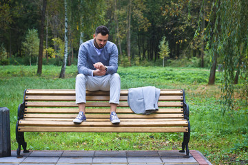 Fototapeta premium Young sexy guy sitting on a bench in an autumnal, summer park. A man contemplating new ideas while walking. European countryside. Stock Photo