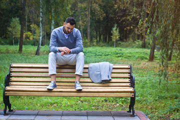 Fototapeta premium Young sexy guy sitting on a bench in an autumnal, summer park. A man contemplating new ideas while walking. European countryside. Stock Photo