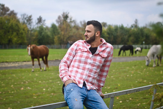 Young handsome guy Cowboy. A man is a farmer at his ranch near the fence. Rural landscapes, countryside. Trees, field, farm. Stock photos