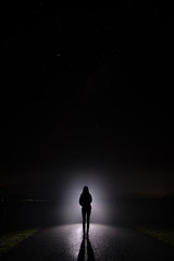 Silhouette of a woman in the darkness. Night Photography. Bright light shining behind dark...